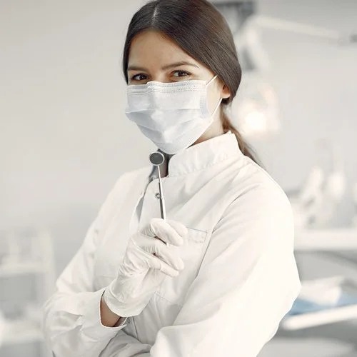 Dentista de jaleco e máscara segurando um espelho clínico